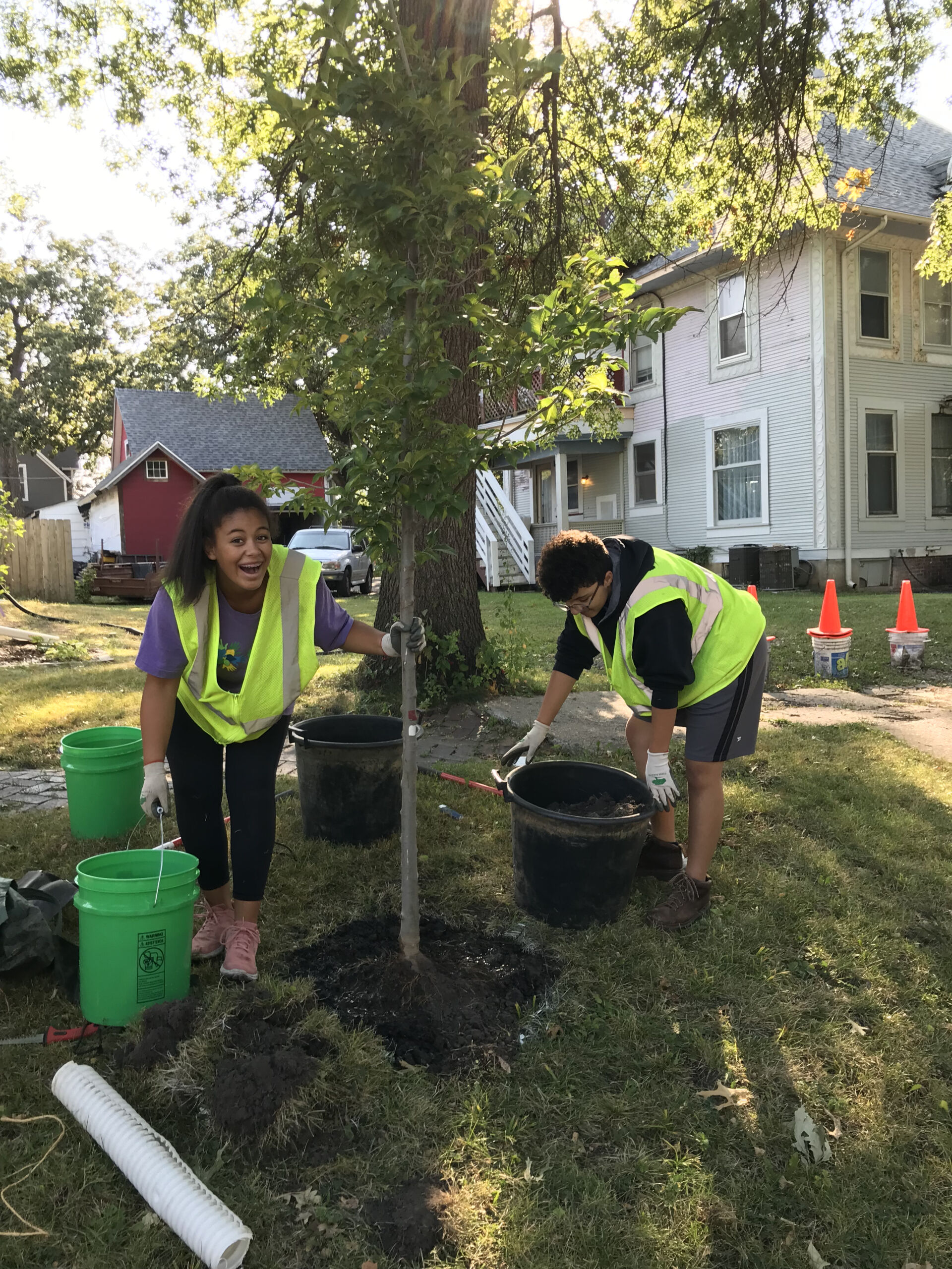 Two young people planting a tree outside a home